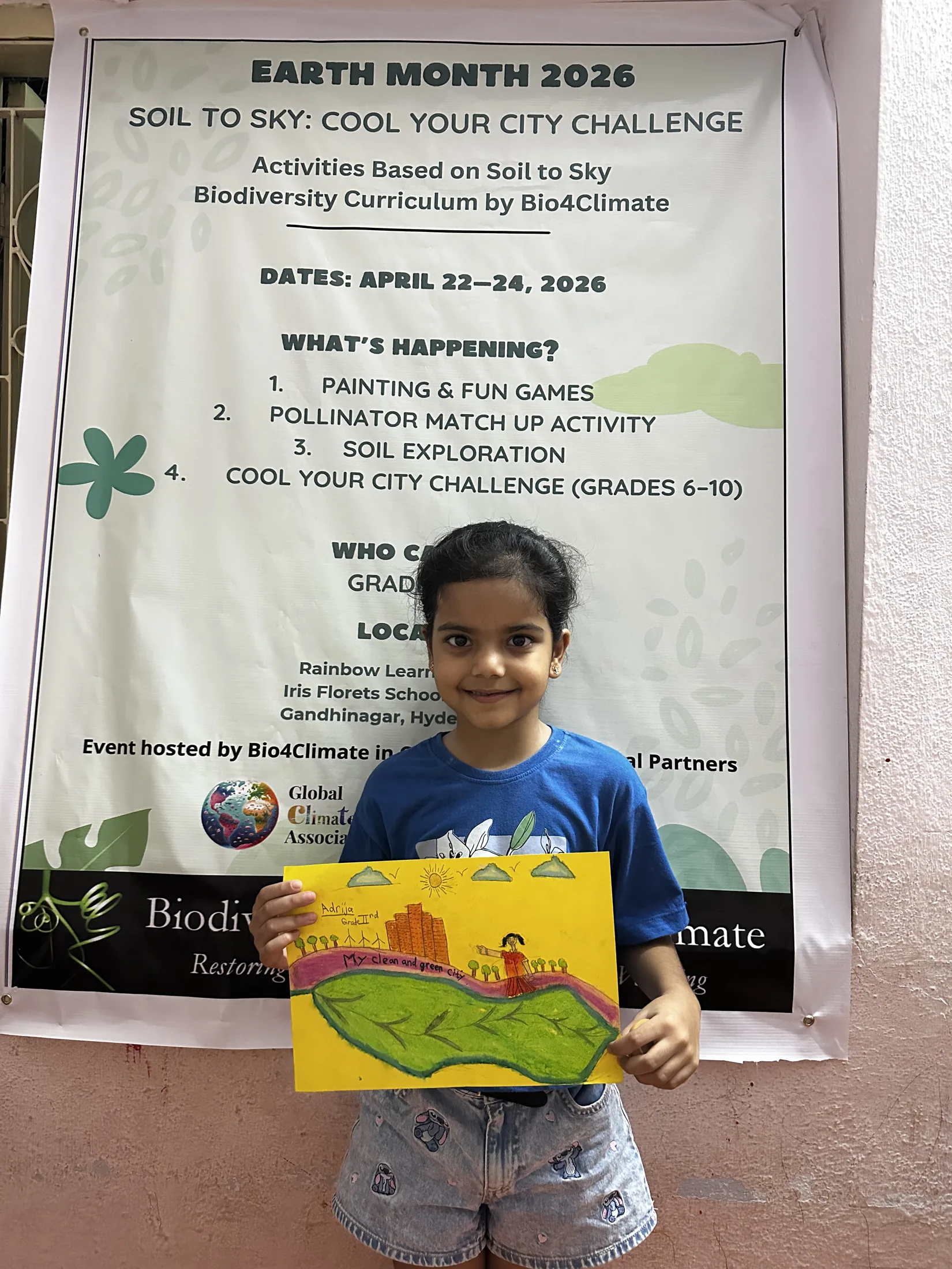 A grade two participant stands with a painting envisioning a green city.